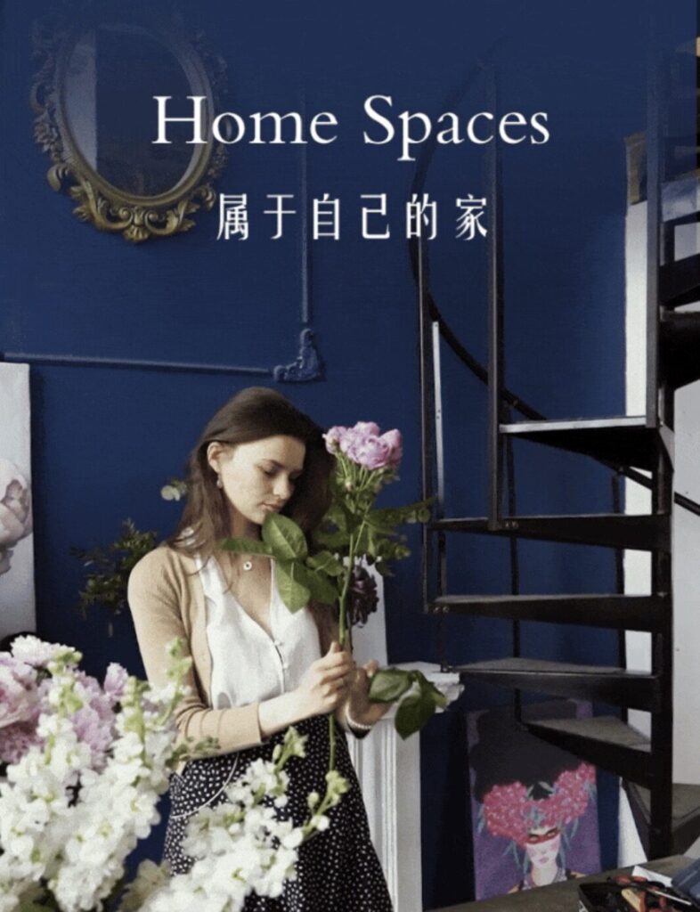 A woman arranges flowers in a room with a spiral staircase and ornate mirror.