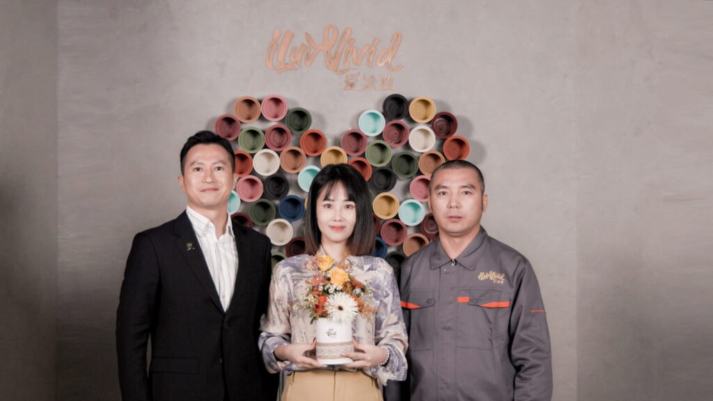 Three people stand in front of a wall decorated with colorful paint pots arranged in a heart shape.
