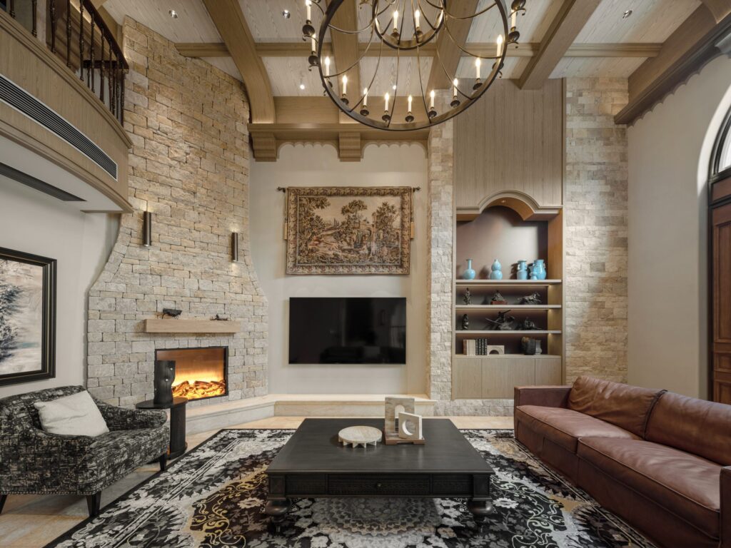 Luxurious living room with a stone fireplace, leather sofa, and ornate chandelier.