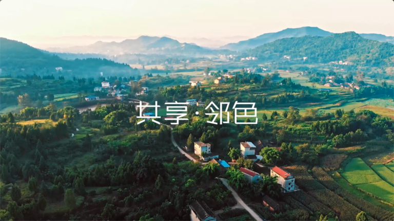 Aerial view of a rural village nestled among lush green hills and misty mountains at sunrise.