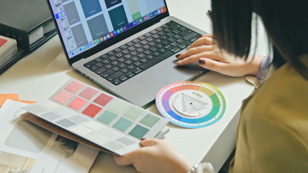 A person uses a laptop and color swatches to select colors for a project.