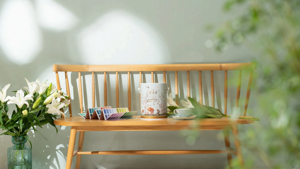 A wooden bench displays paint swatches, a decorative can, and white lilies against a soft green wall.