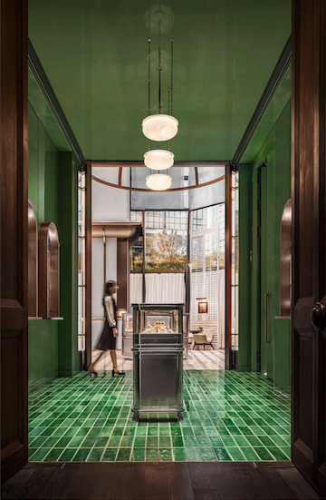 A woman walks past a display case in a hallway with green walls and tiled floor.