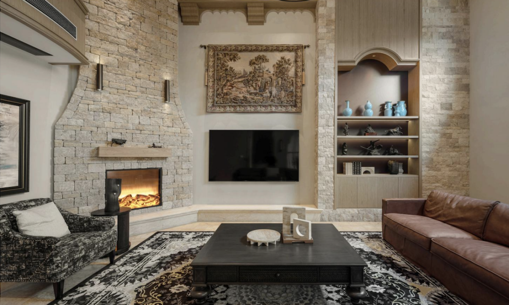 A Tuscan-style living room features a stone fireplace, tapestry, and a brown leather sofa.
