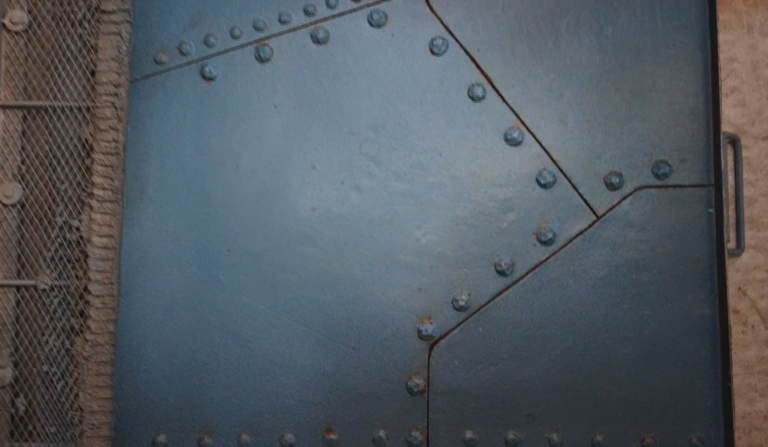 Riveted navy metal panels form a textured surface with a metal handle on the right.