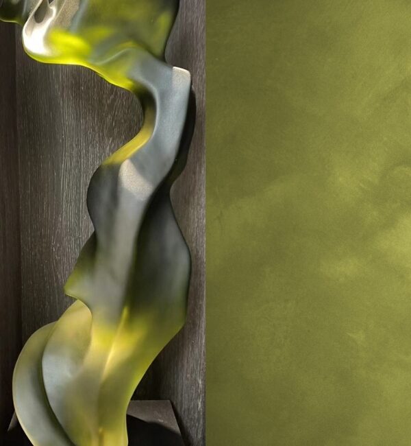 A flowing, translucent glass sculpture with a textured olive green background.
