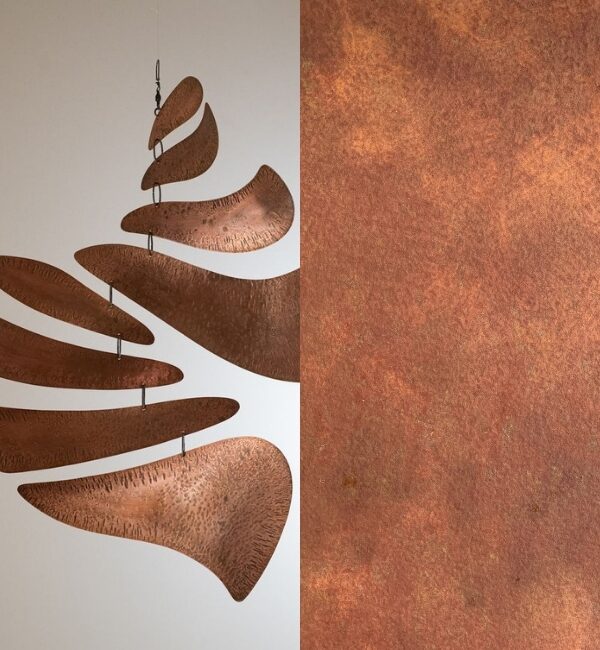 A copper mobile with curved, textured elements hangs against a white background next to a textured copper surface.