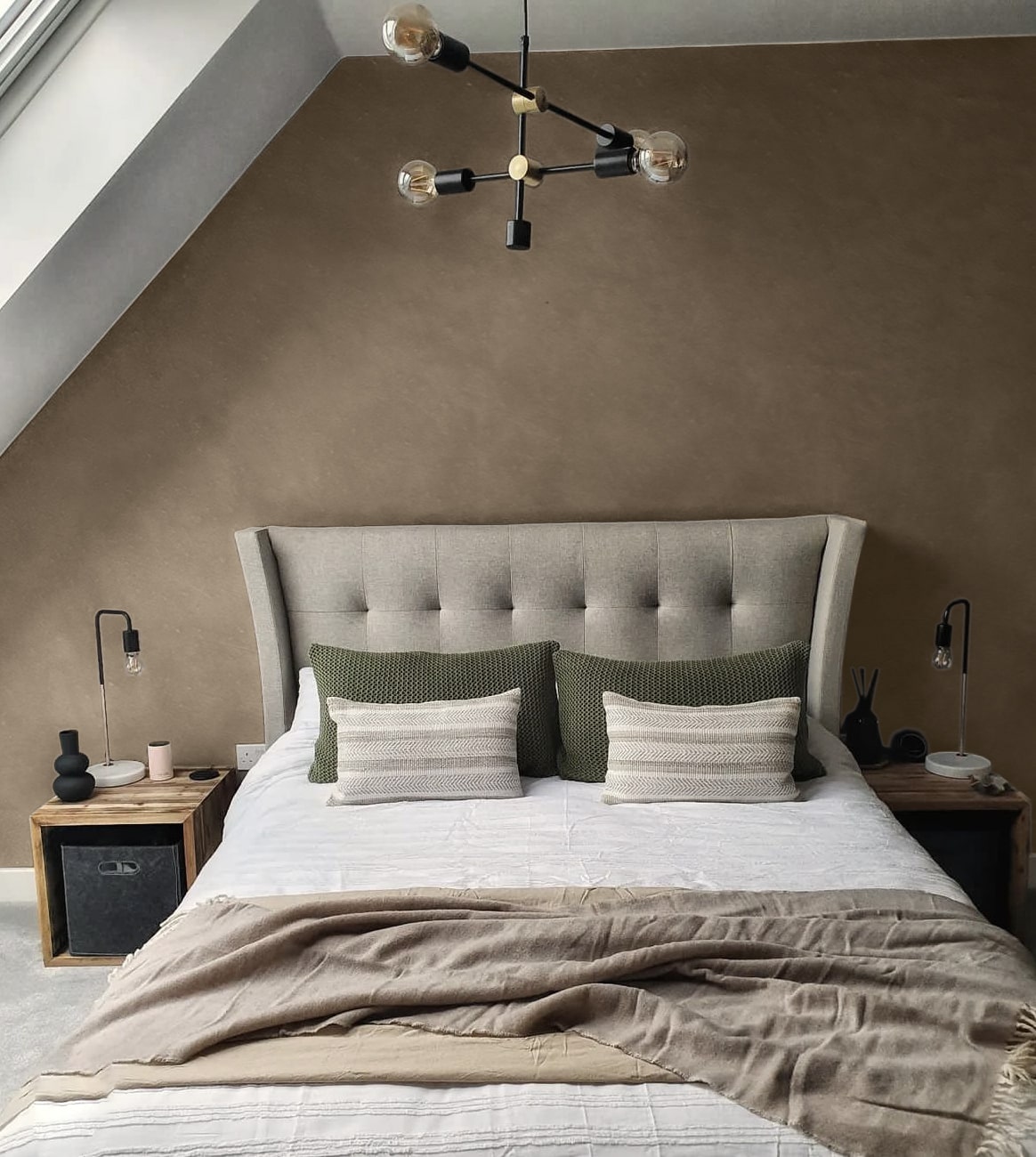 A cozy bedroom features a tufted headboard, layered pillows, and a textured throw blanket.