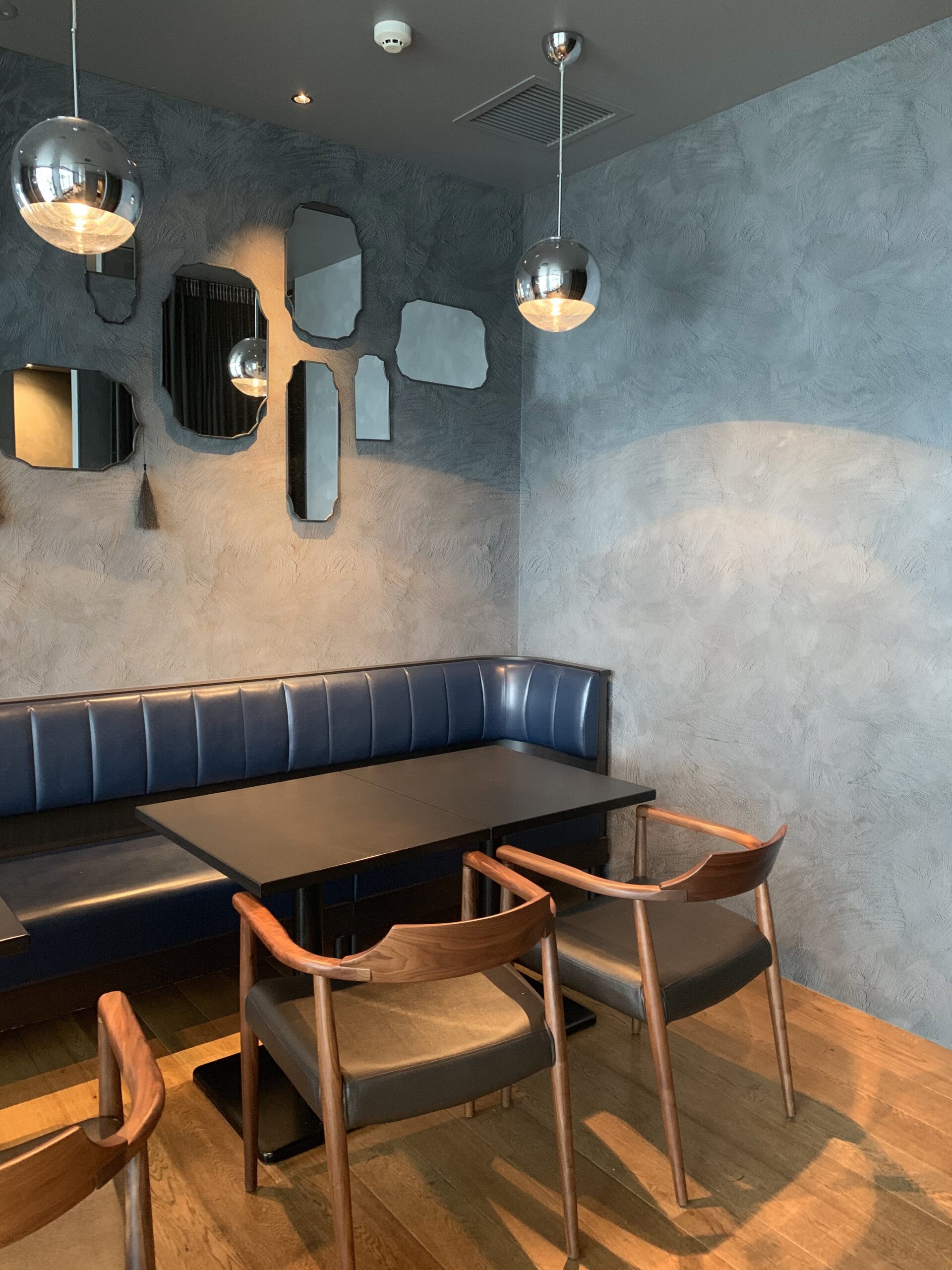 Modern dining area with a blue banquette, dark table, and wooden chairs against a textured gray wall.