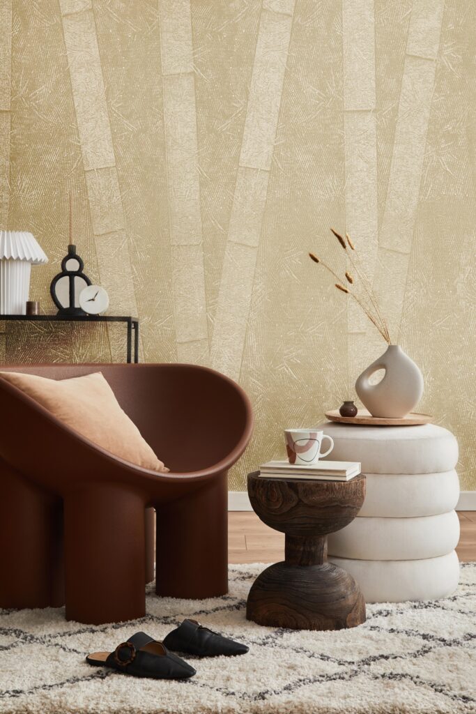 A modern living room features a brown chair, white poufs, and a textured gold wallpaper.