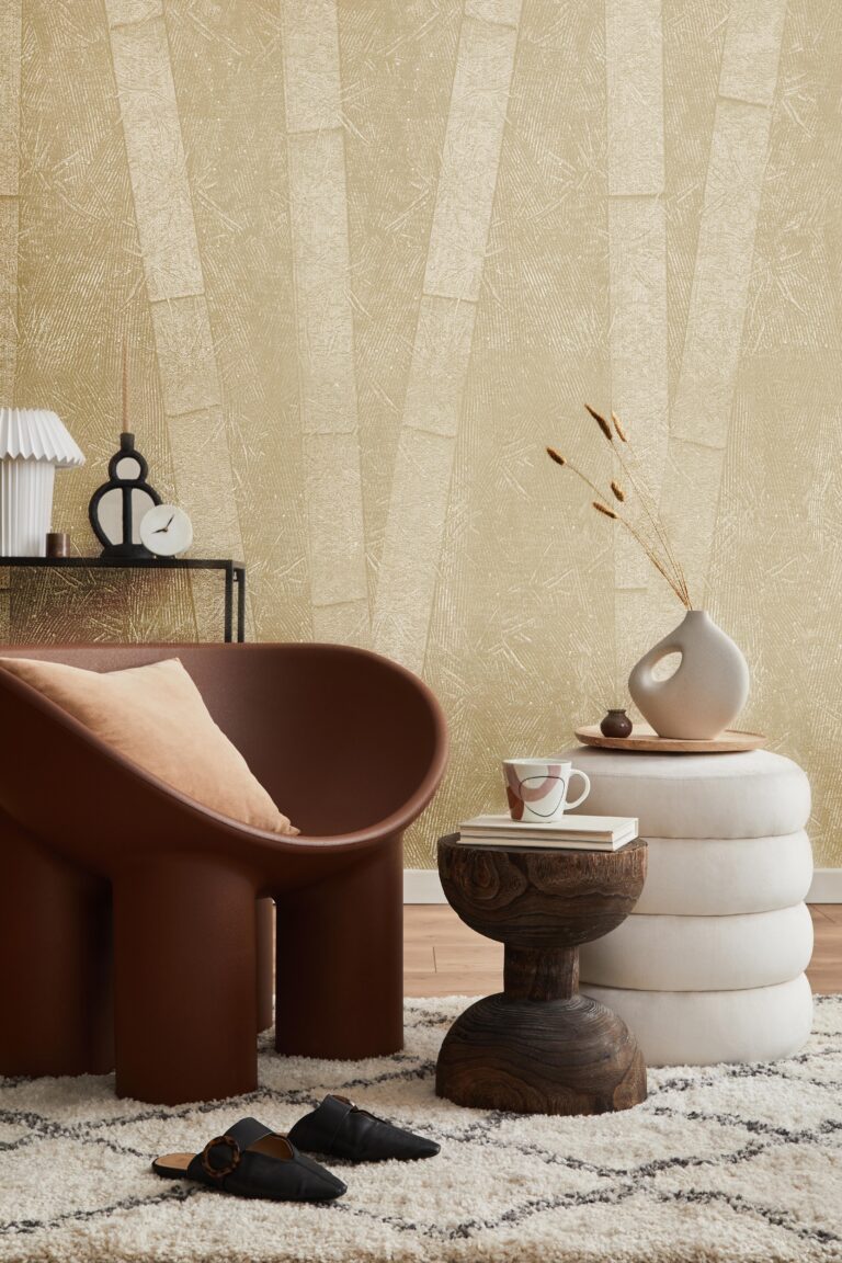 A modern living room features a brown chair, white poufs, and a textured gold wallpaper.