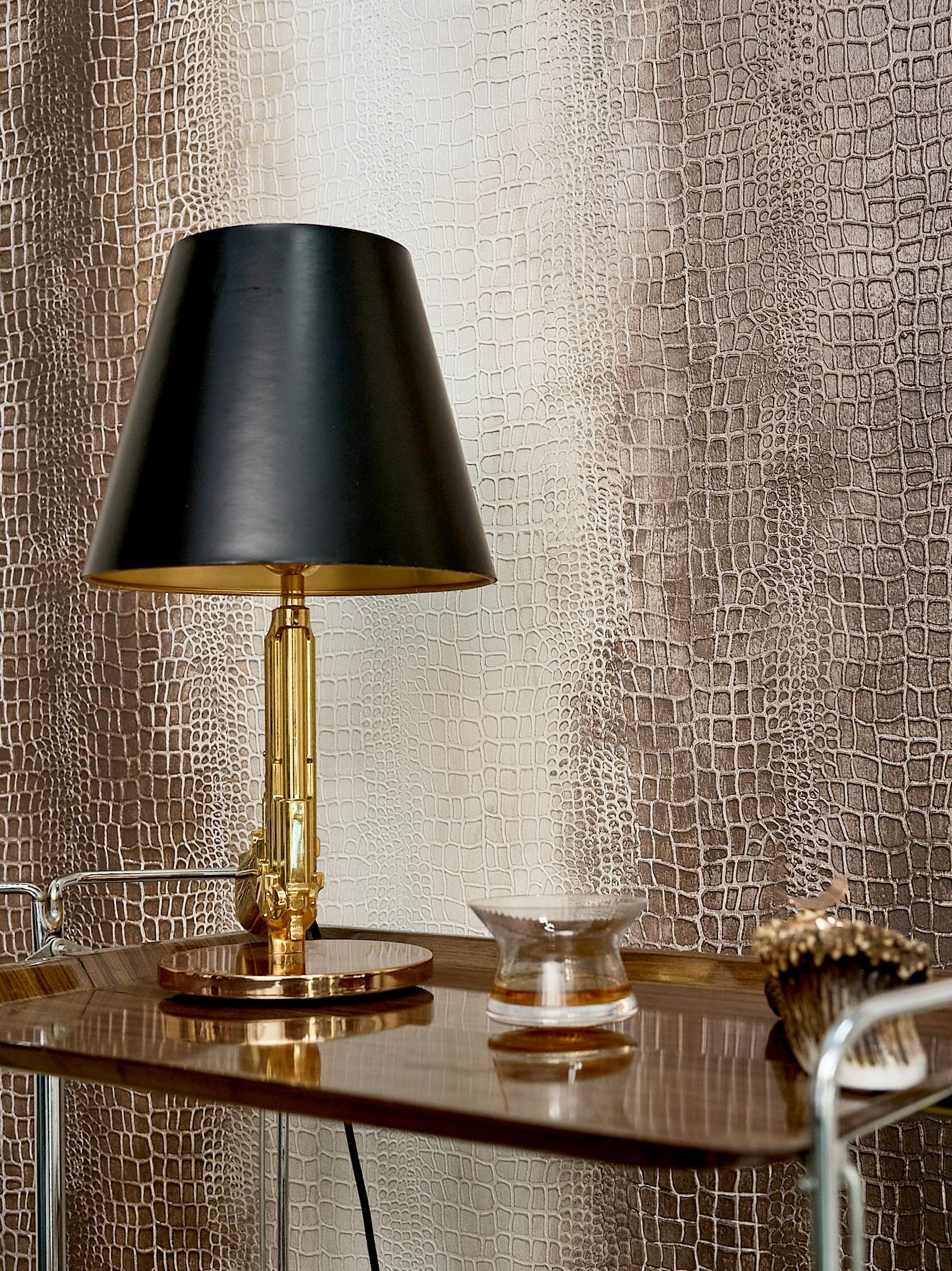 A gold lamp with a black shade sits on a bar cart against a textured animal print wallpaper.