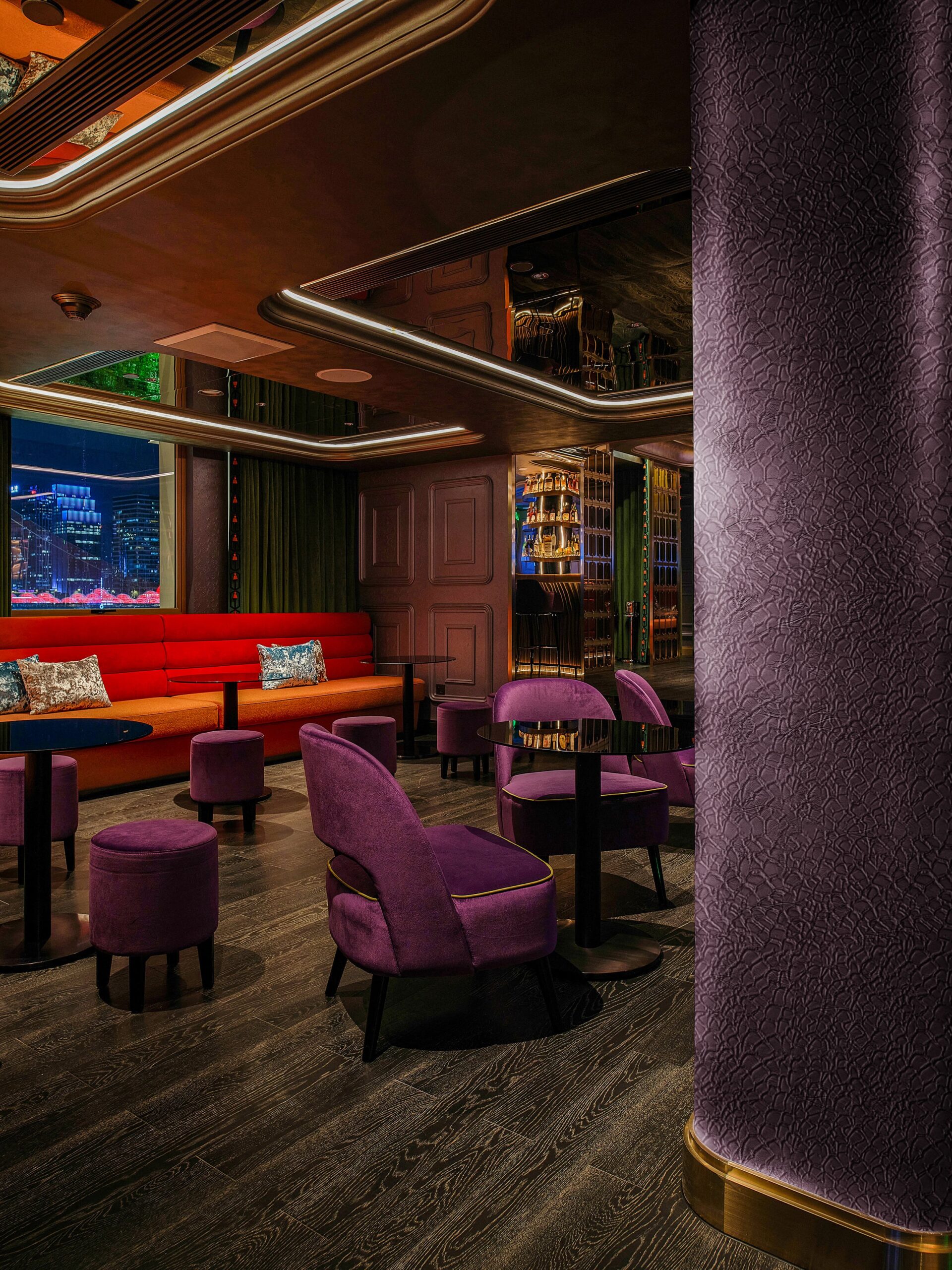 Plush purple seating and dark wood floors create a luxurious lounge with city views.