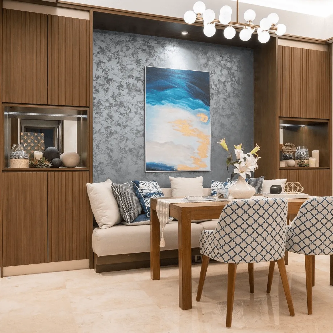 A dining area features a wooden table and chairs with a blue geometric pattern, set against a textured wall with abstract art.