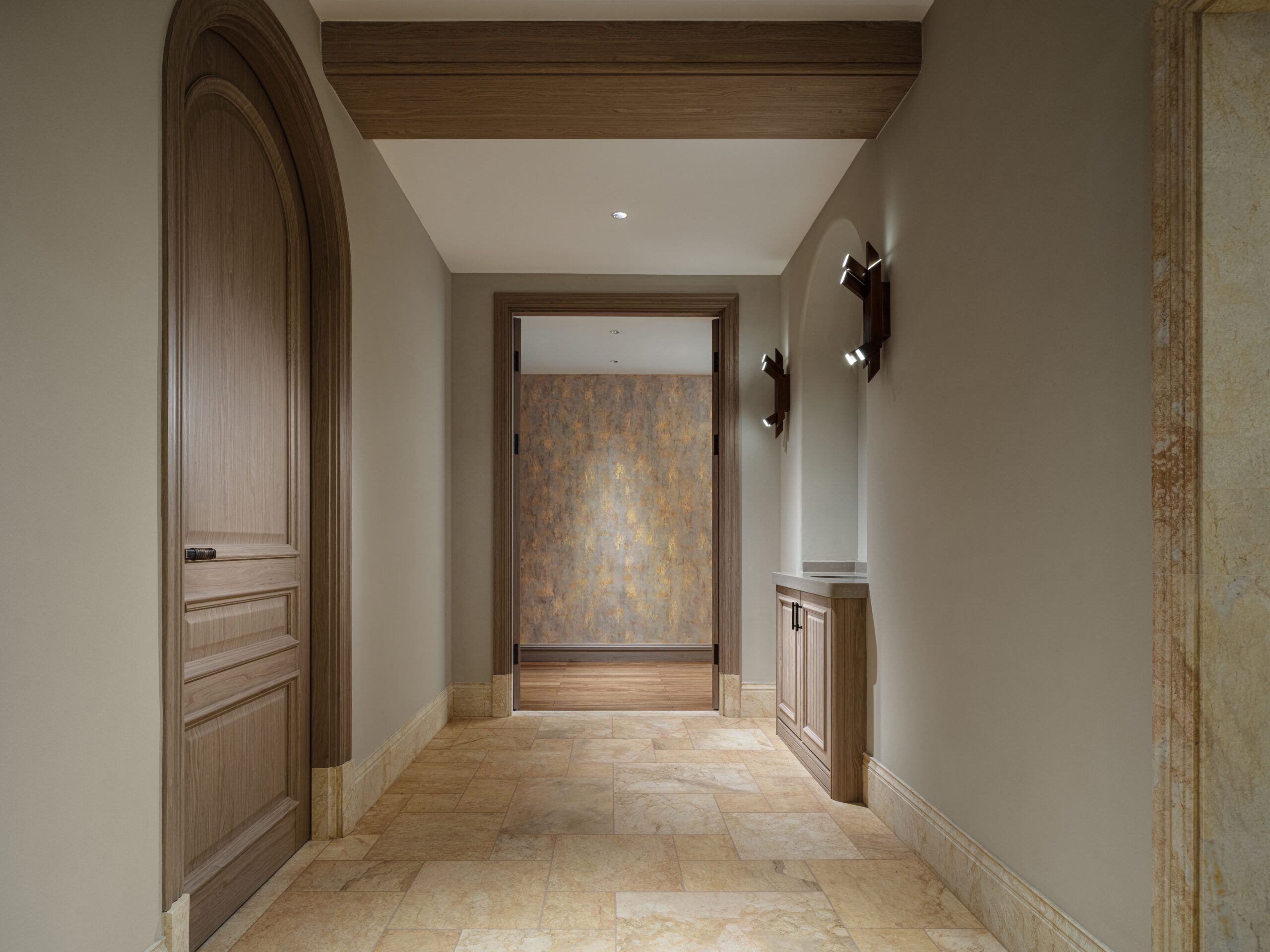 A hallway with arched wooden doors, stone tile flooring, and decorative wall sconces.