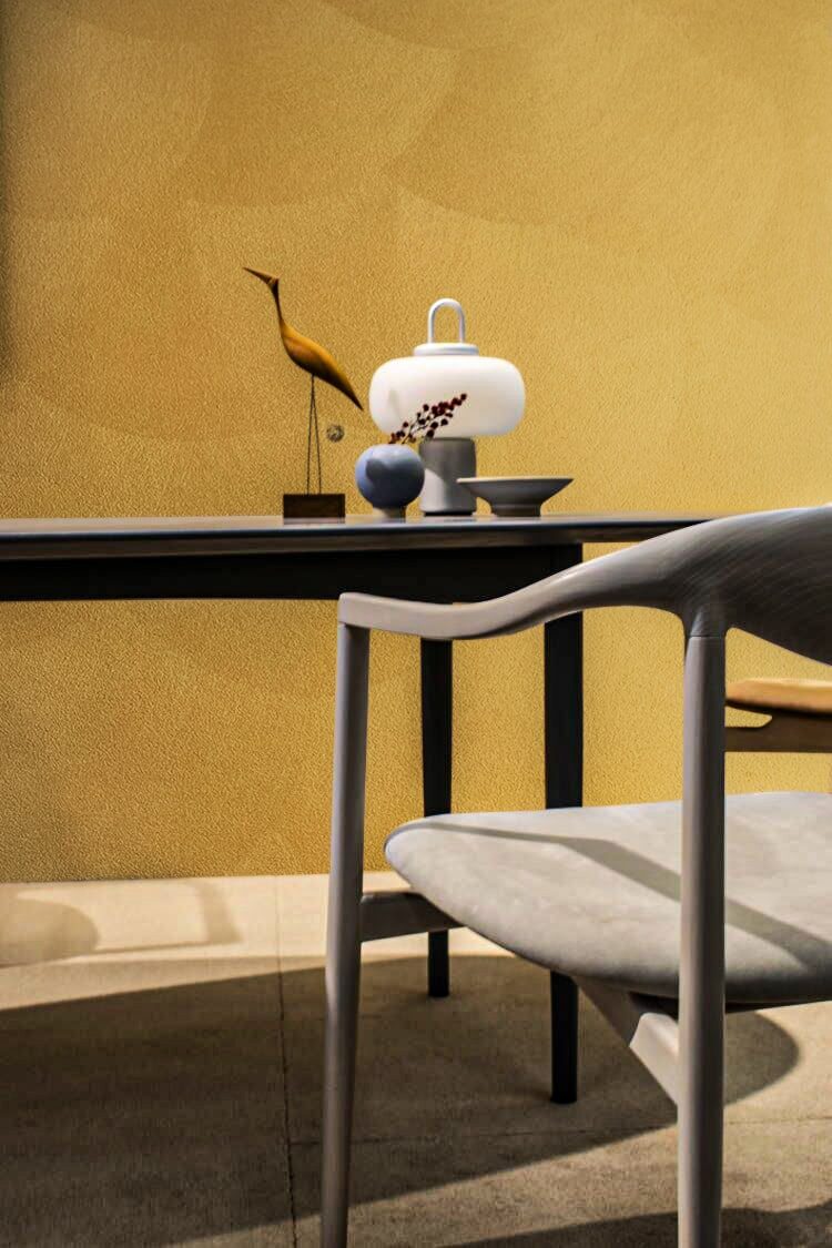A modern gray chair sits before a dark table with decorative objects against a textured yellow wall.
