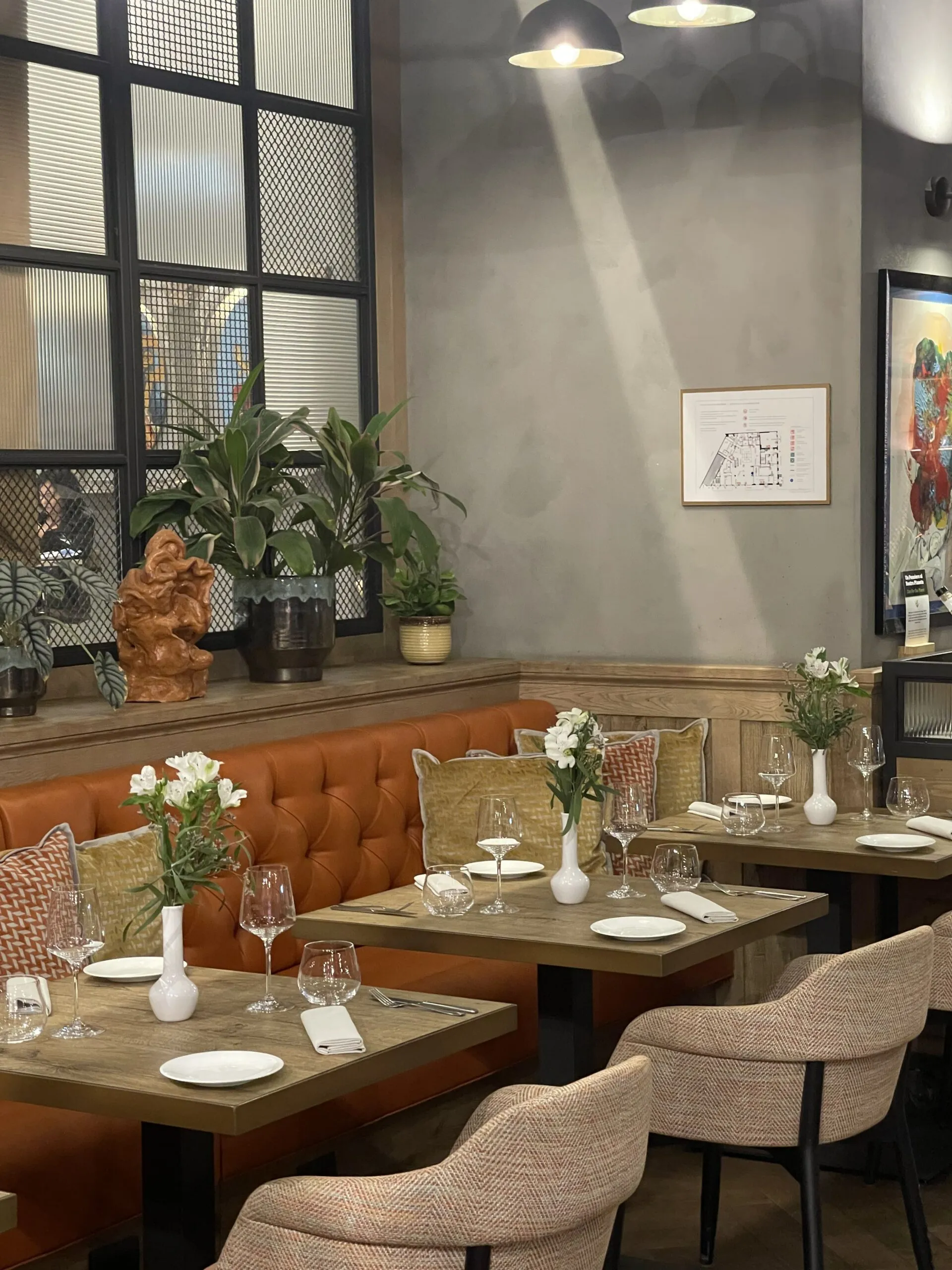 Elegant dining tables are set with white flowers and glassware in a restaurant with plush seating.
