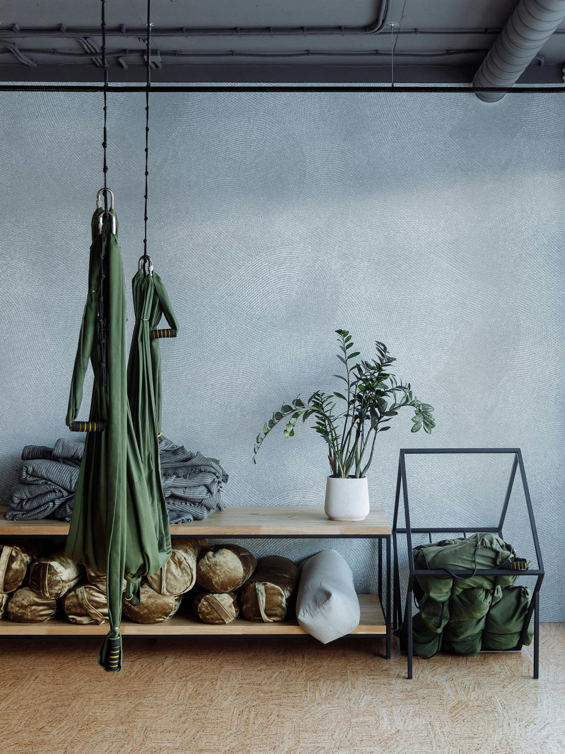 Green aerial yoga hammocks hang above shelves filled with bolsters and blankets in a studio.