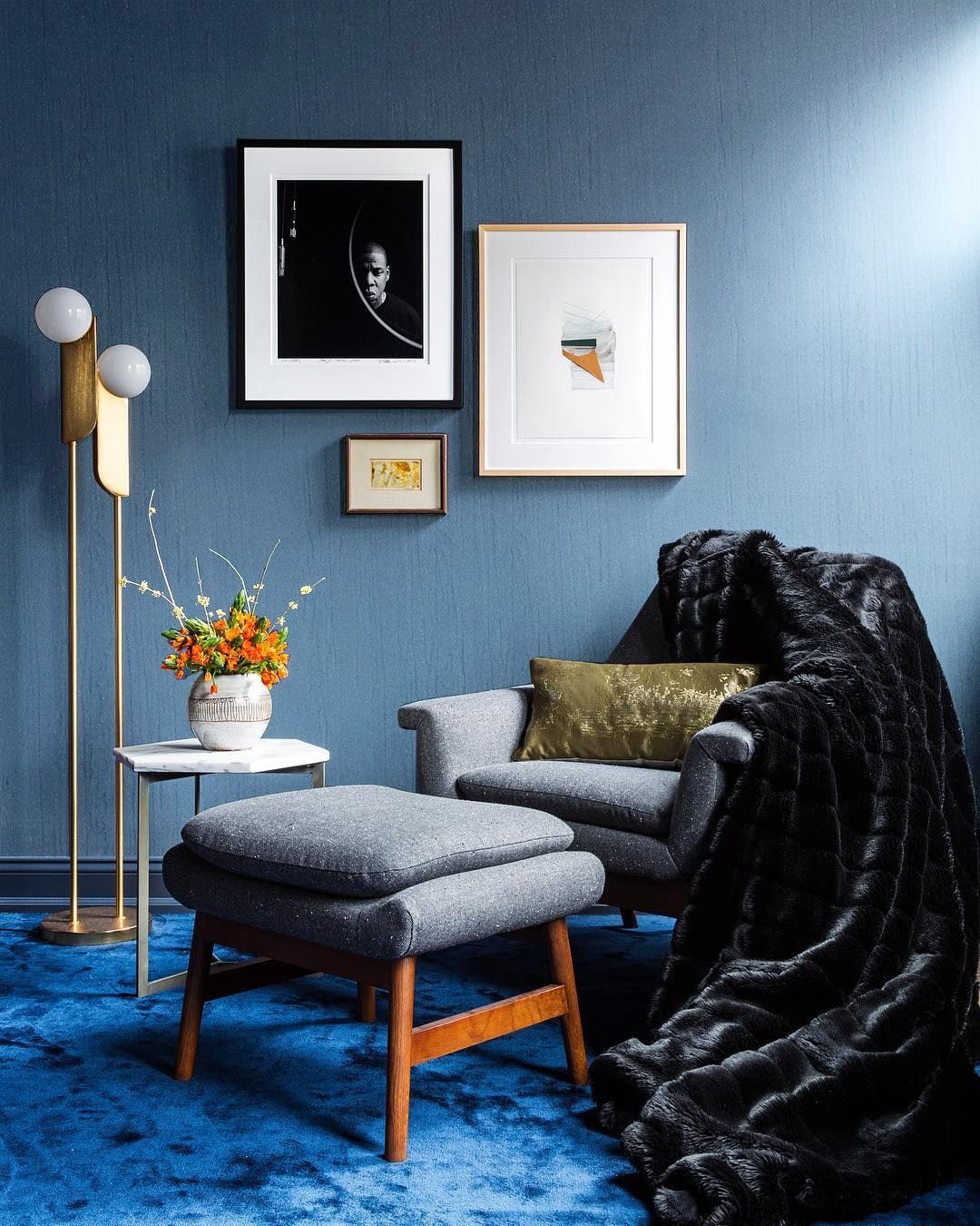 A grey armchair with a black faux fur throw sits on a blue rug next to framed art.