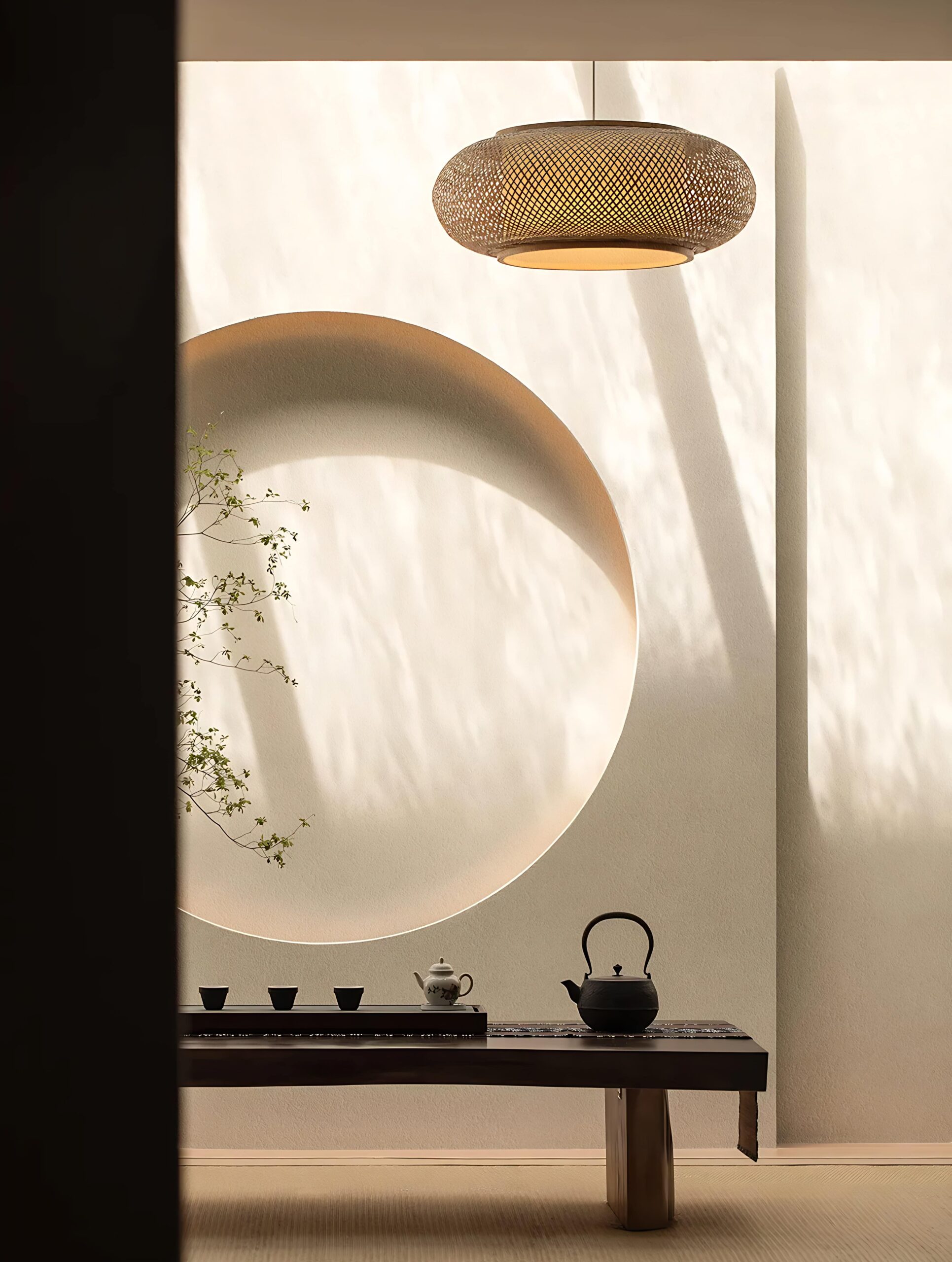 A minimalist tea set rests on a dark wooden table against a textured wall with a circular cutout.