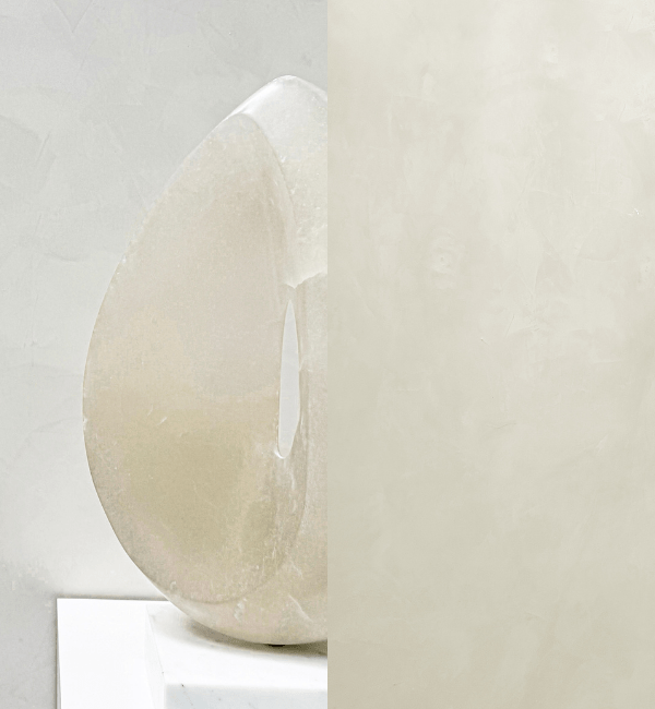 A translucent, polished marble sculpture rests on a white pedestal against a textured wall.