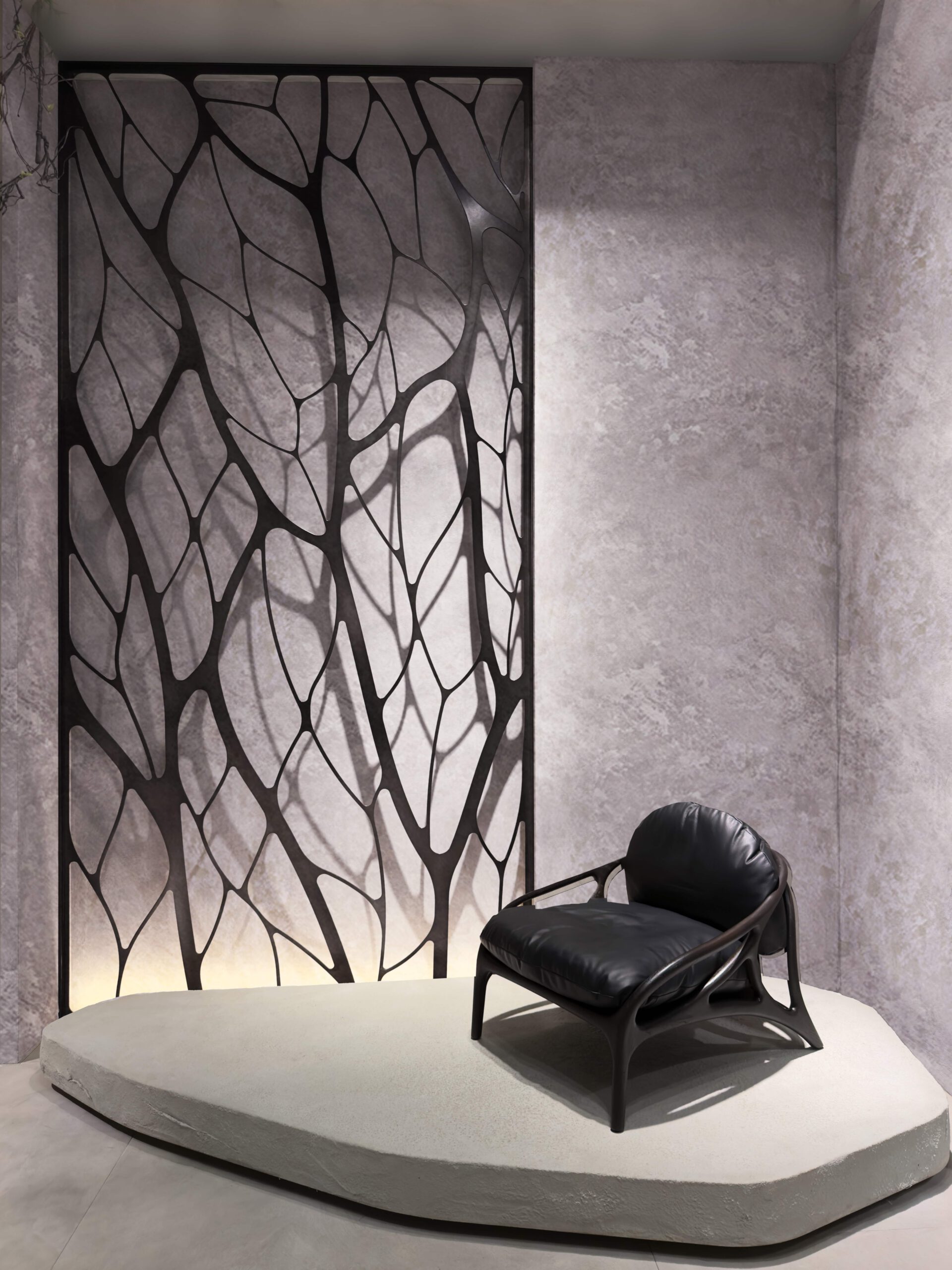 A black leather armchair sits on a concrete pedestal before a decorative screen with a tree-like pattern.