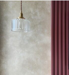 A clear glass pendant light hangs in a room with textured walls and a ribbed pink accent wall.
