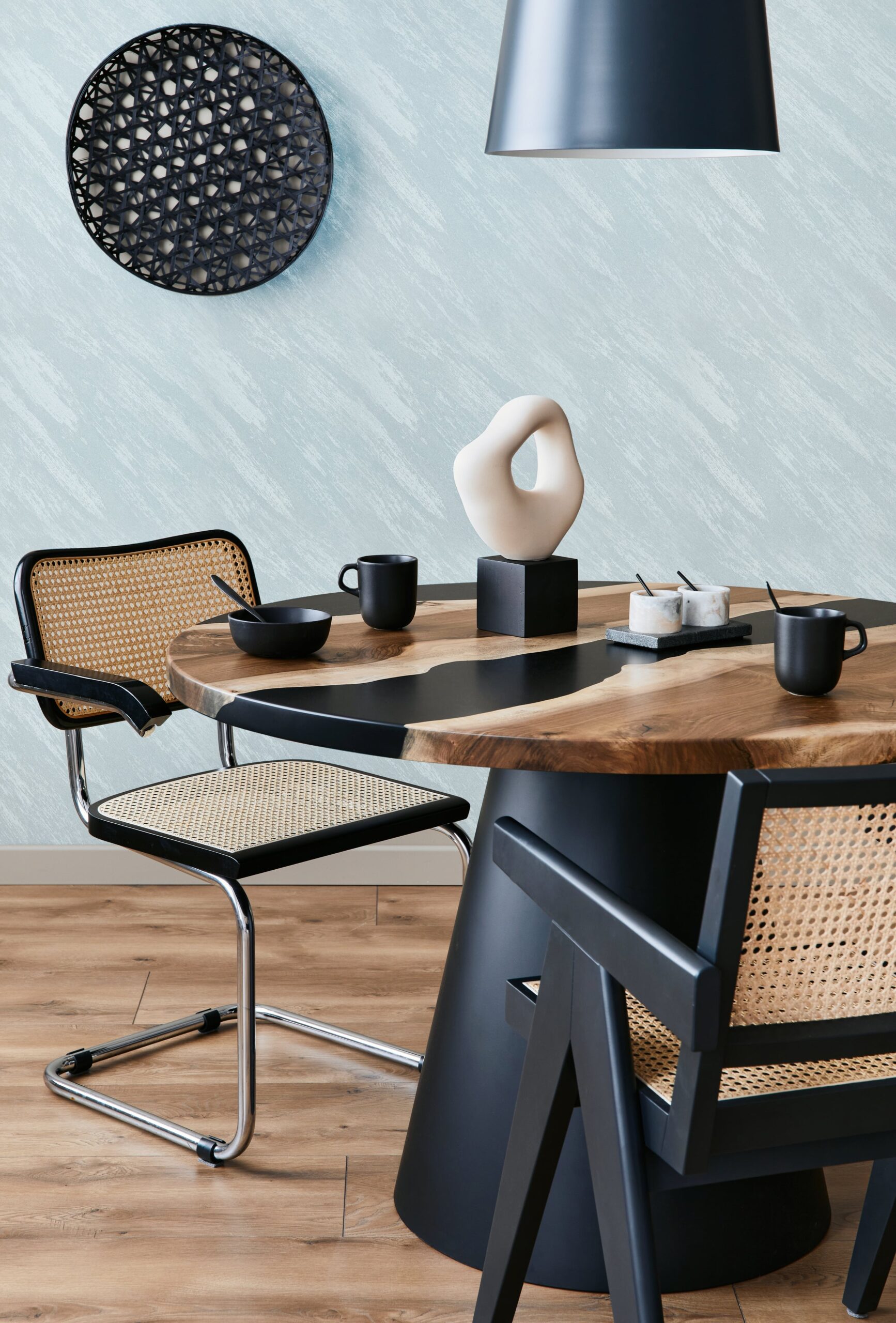 A round wooden table with a black leopard print inlay is set with black mugs and a sculpture.