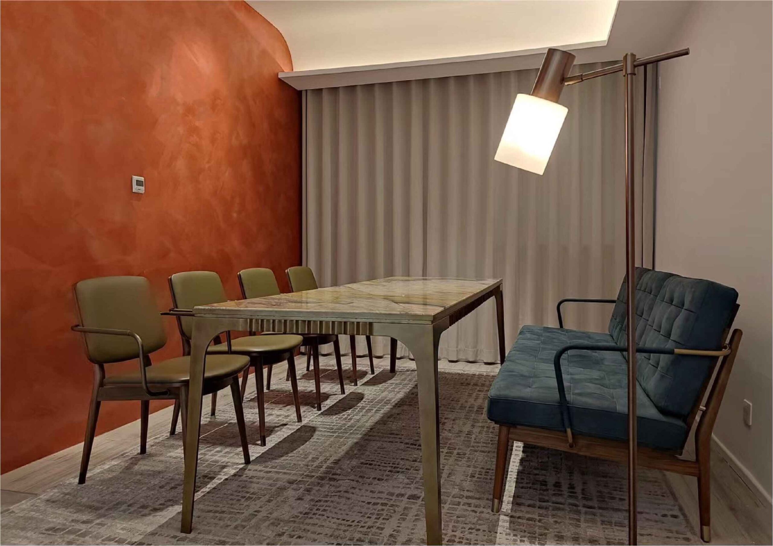A dining room with a marble table, green chairs, and a blue sofa under a floor lamp.