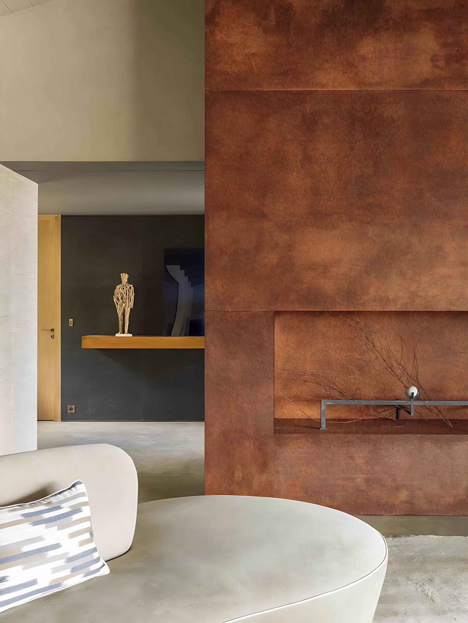 A modern living room features a textured copper fireplace, a minimalist sculpture, and a rounded sofa with a patterned cushion.