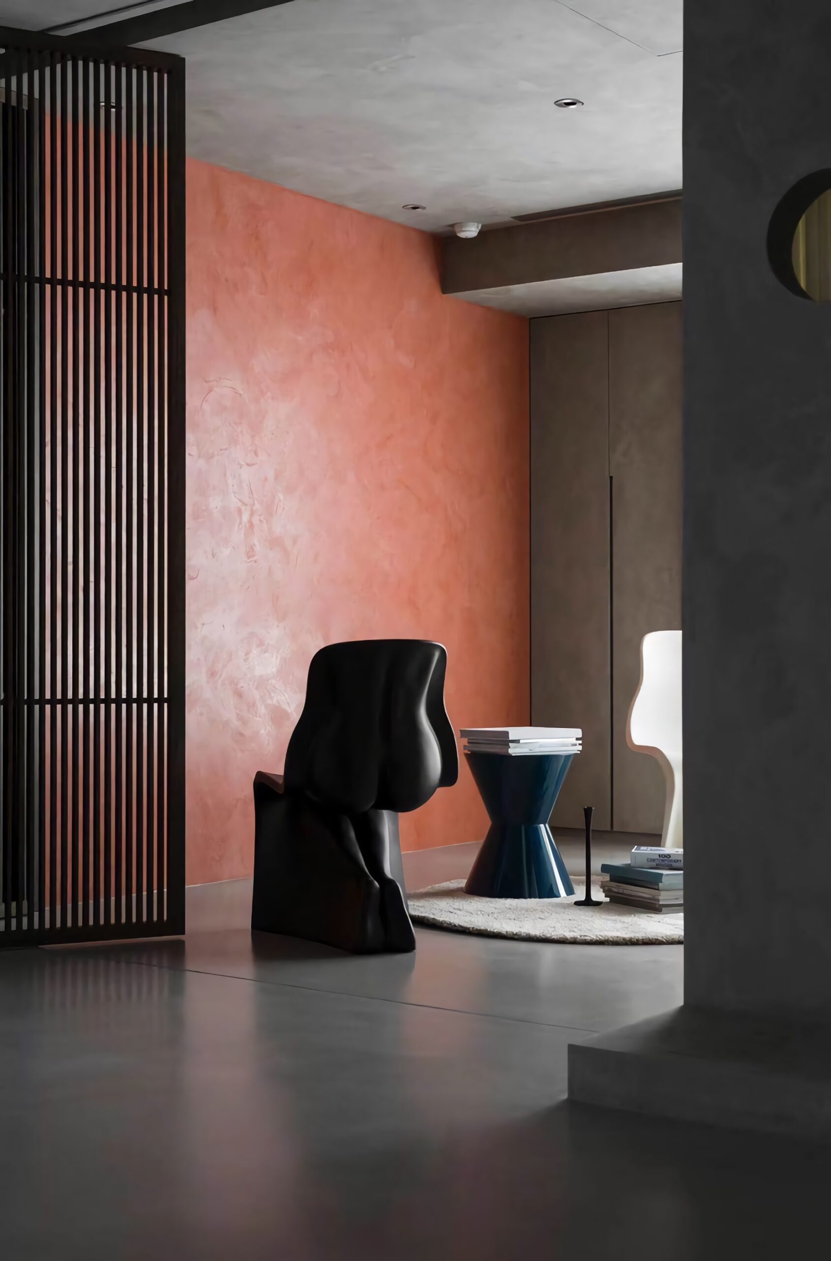 A black sculptural chair sits in a modern room with a coral-textured wall.